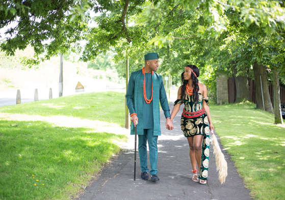 Bride and groom in traditional Nigerian clothing holding hands and smiling at each other while walking along path